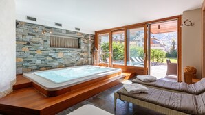 A spa area with a stone wall, a hot tub, and a seating area with a view of the outdoors. - Sottovento Luxury Hospitality (Bormio)