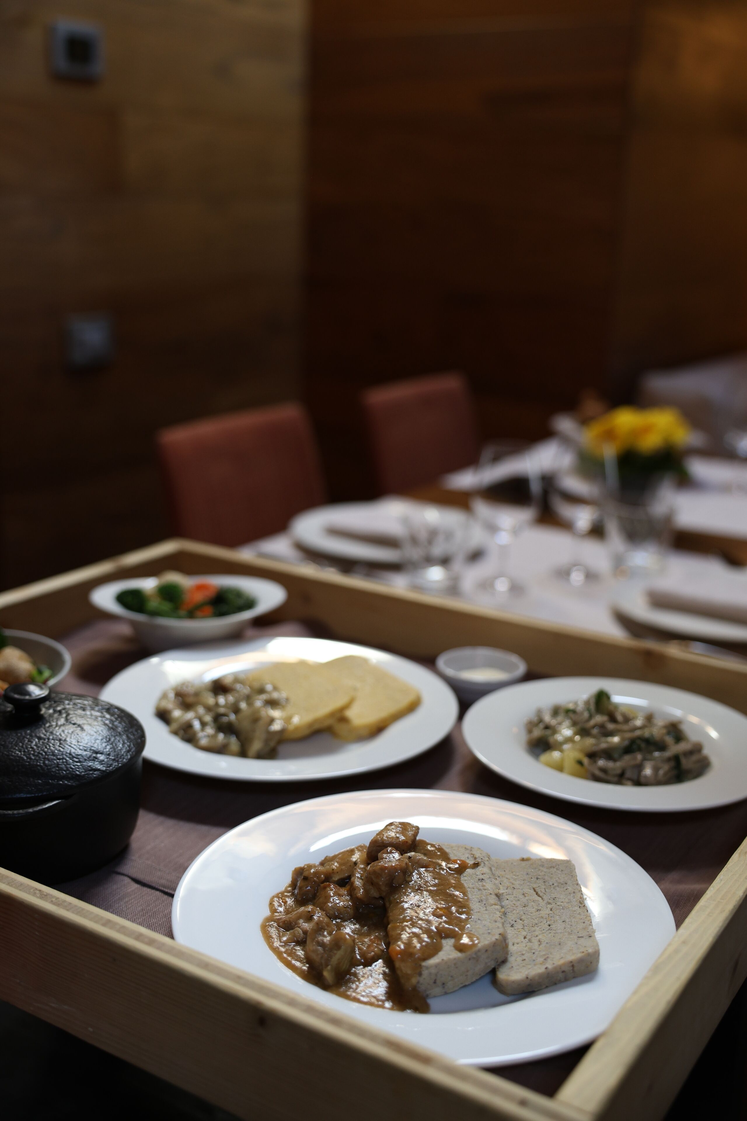 A dining table with various dishes, including a plate with meat and sauce, a bowl of vegetables, and a plate with a bread-like item.