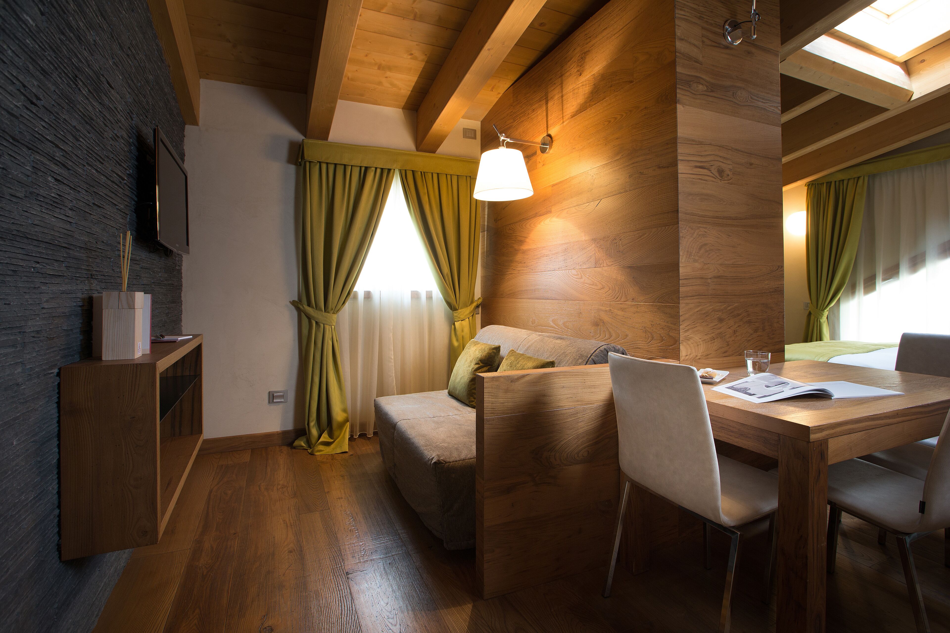 Una habitación acogedora con techo de madera, un sofá, una mesa de comedor con sillas y un televisor montado en la pared.