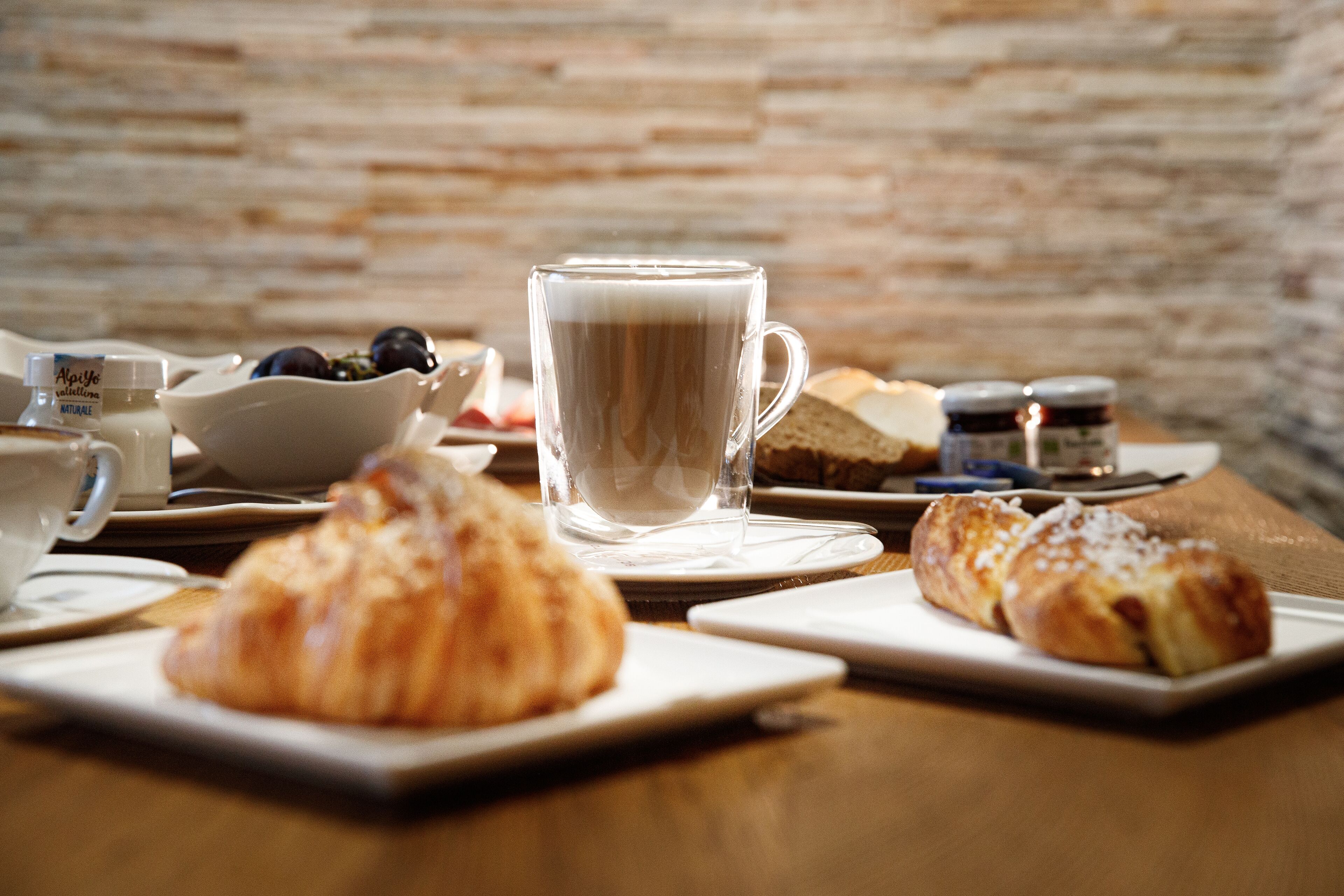 A breakfast setting with croissants, a cup of coffee, and a bowl of fruit on a wooden table.