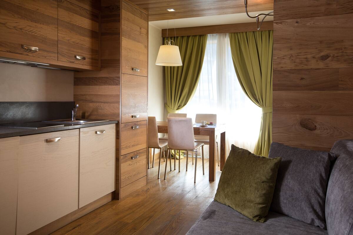 Una cocina compacta con armarios de madera, una zona de comedor con mesa y sillas, y un sofá con cojines.