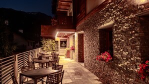 An outdoor patio with tables and chairs, a stone wall with flowers, and a mountain backdrop. - Sottovento Luxury Hospitality (Bormio)