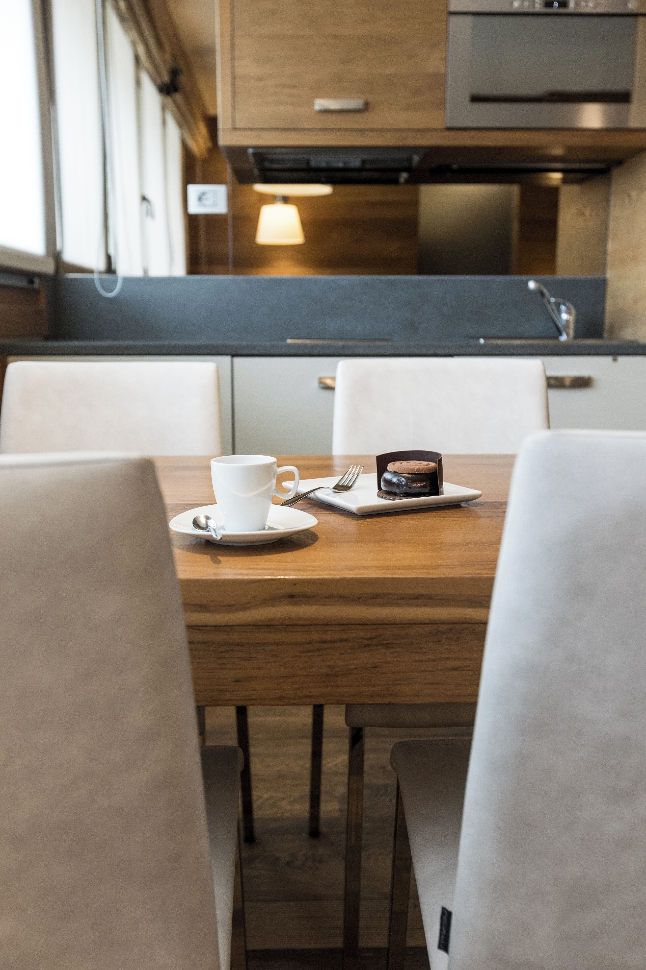 A wooden dining table with a white cup and a small dessert on a plate, surrounded by white chairs.