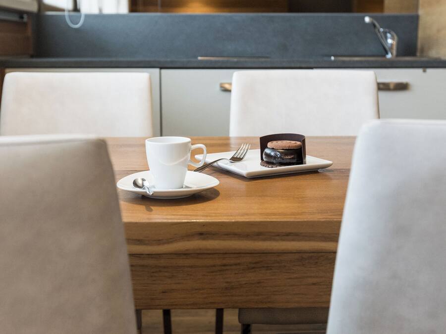 A wooden dining table with a white cup and a small dessert on a plate, surrounded by white chairs.