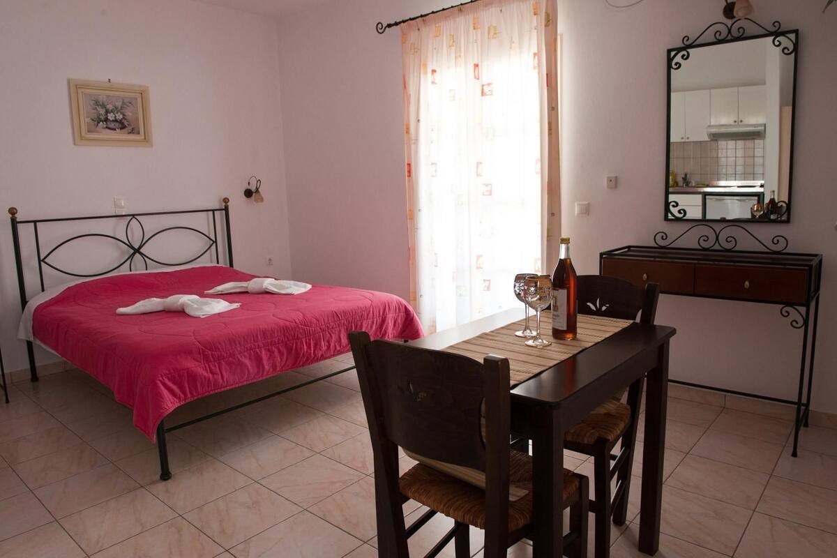 A bedroom with a bed, a desk, and a chair. There is a bottle of wine and two glasses on the desk.