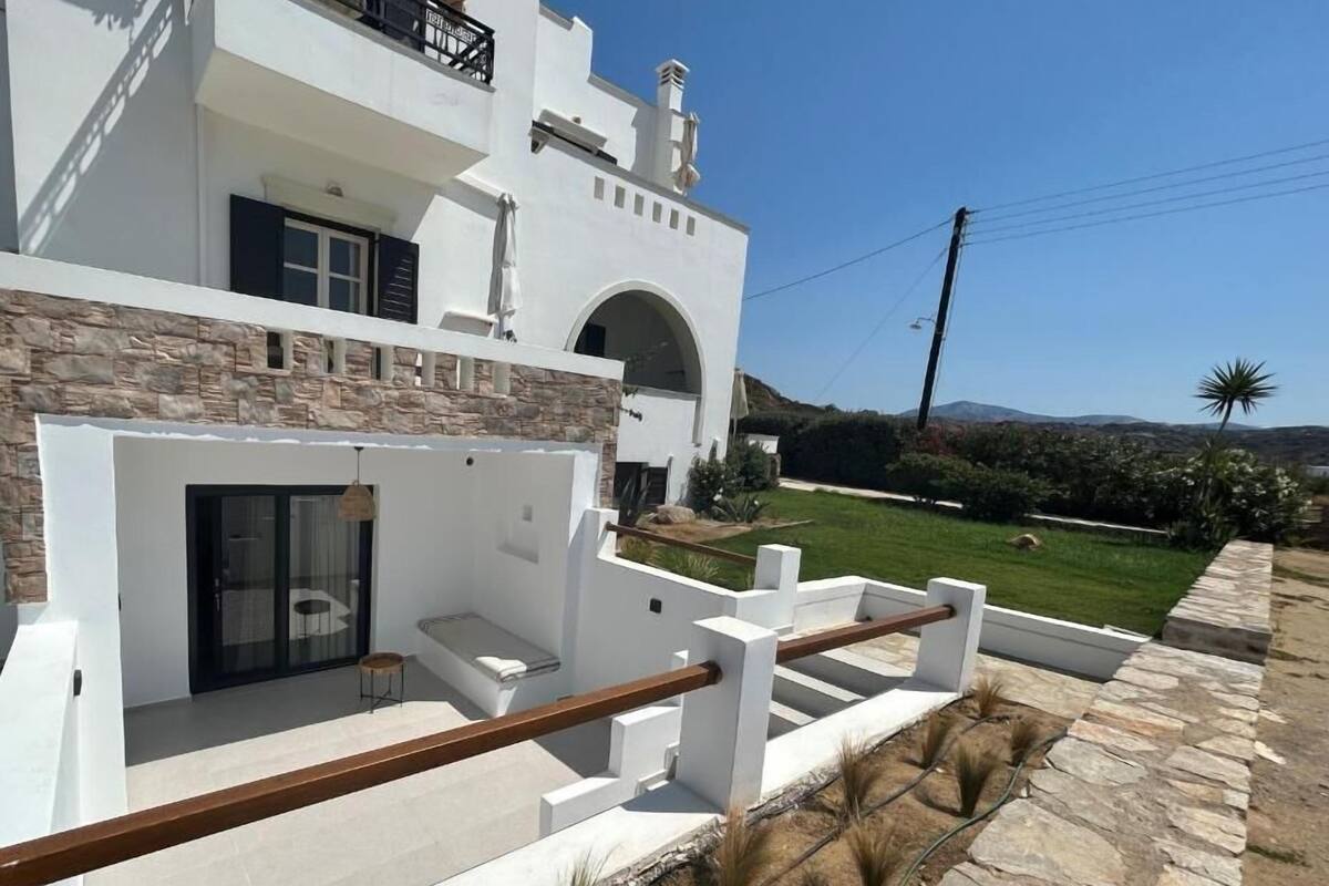 A modern house with a stone facade, a balcony with a wooden railing, and a view of a green landscape with hills in the background.