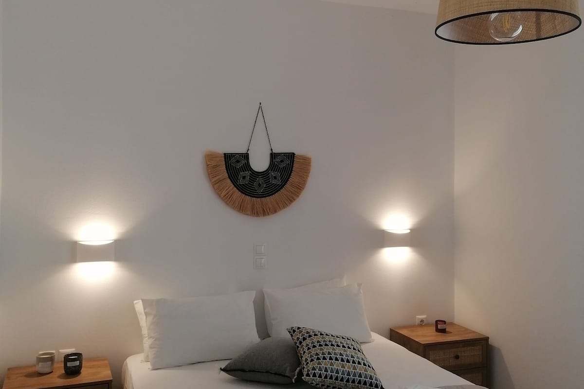 A bedroom with a bed, two bedside tables, a wall-mounted light fixture, and a hanging light.