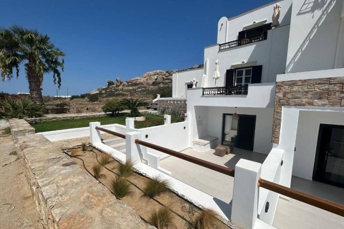 A modern white building with a balcony, stone walls, and a view of the landscape.