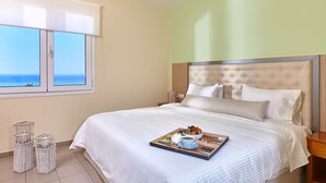 A neatly made bed with a tray of breakfast items, a view of the sea through the window, and a simple, clean room design. - Everest Apartments (Hersonissos)