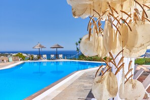 A swimming pool with lounge chairs and umbrellas, overlooking the ocean.