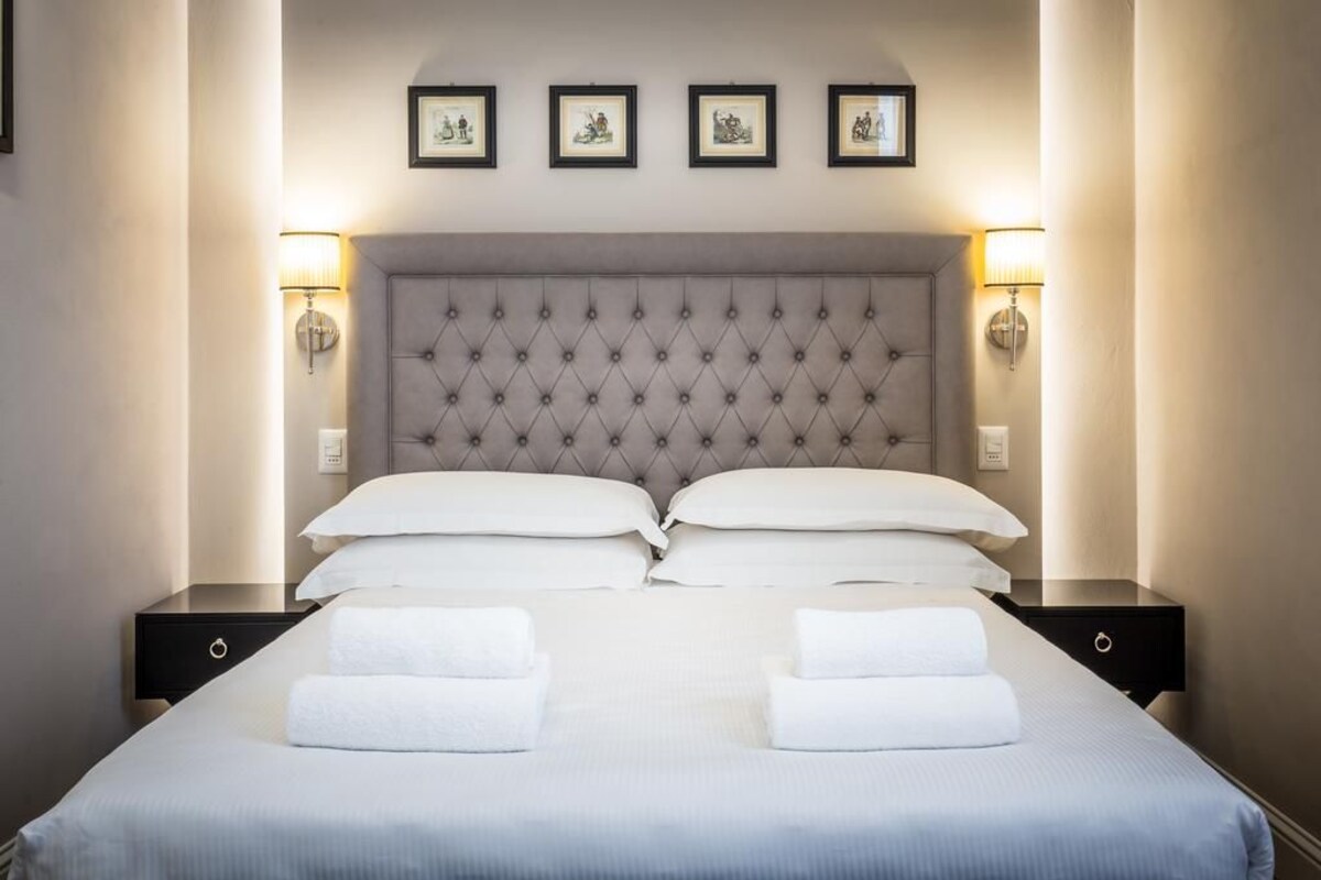A neatly made bed with a tufted headboard, two bedside tables, and wall-mounted lamps.