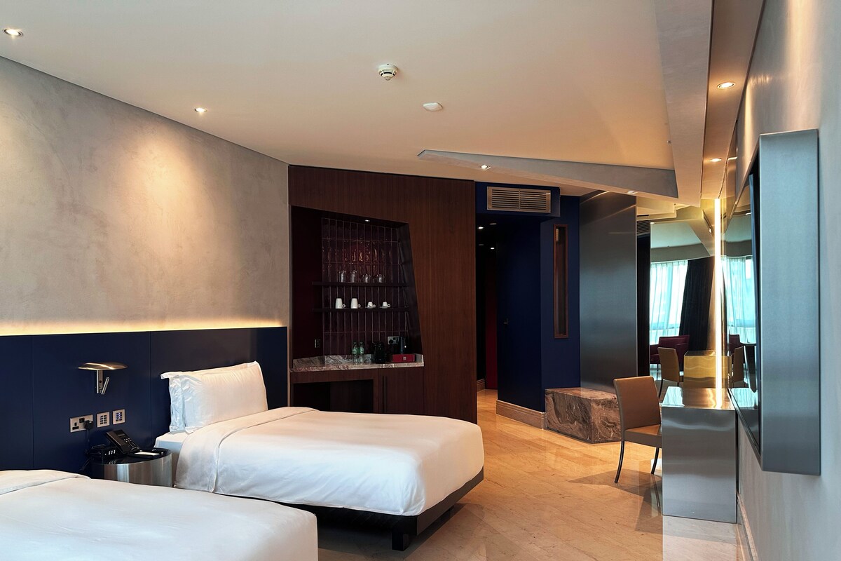 Ein modernes Hotelzimmer mit zwei Betten, einer Sitzecke und einer Minibar.