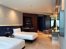 A modern hotel room with two beds, a seating area, and a minibar.