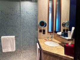 Un baño con cabina de ducha de vidrio, un lavamanos con encimera de mármol y dos espejos con marco azul fijados a la pared.