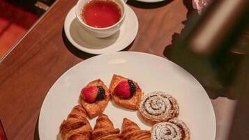 A breakfast tray with croissants, a rolled pastry, and a cup of tea on a wooden table.