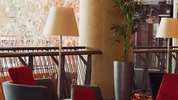 A modern lobby with a seating area featuring red and grey chairs, a large plant, and a decorative lamp.