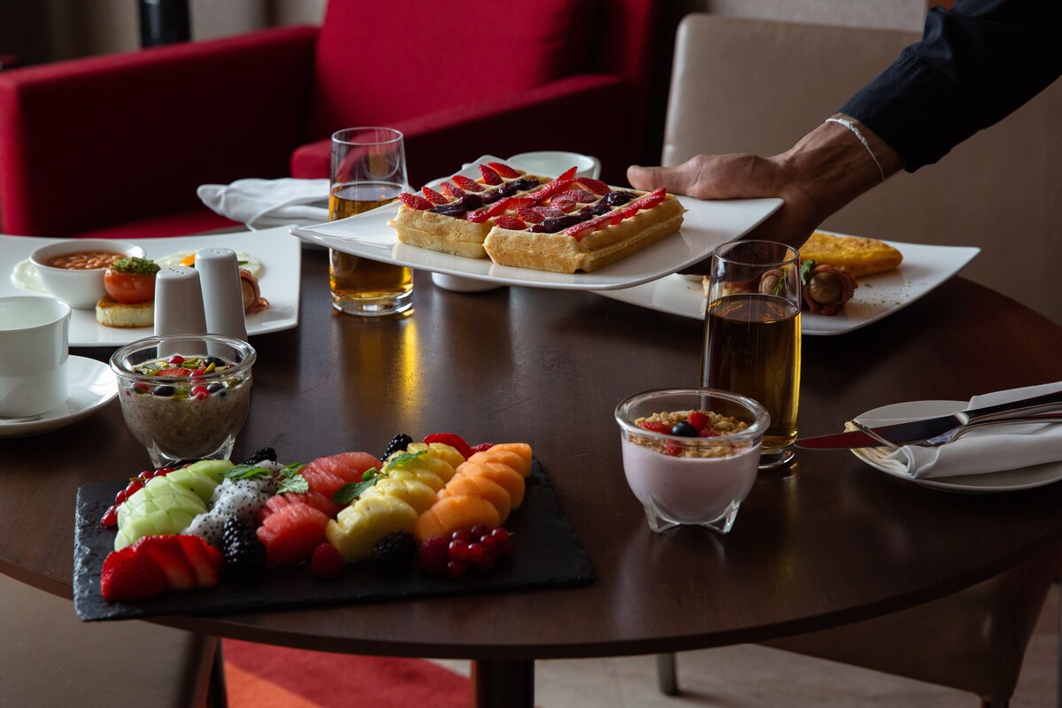 Une table à manger où l’on trouve une variété de plats, notamment des gaufres, des fruits et un dessert.