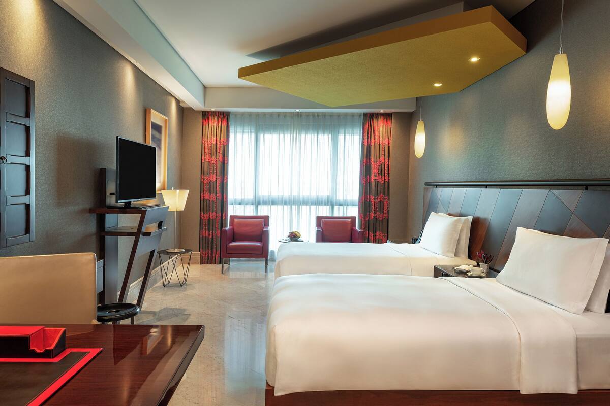 A hotel room with two beds, a TV, a desk, and a chair.