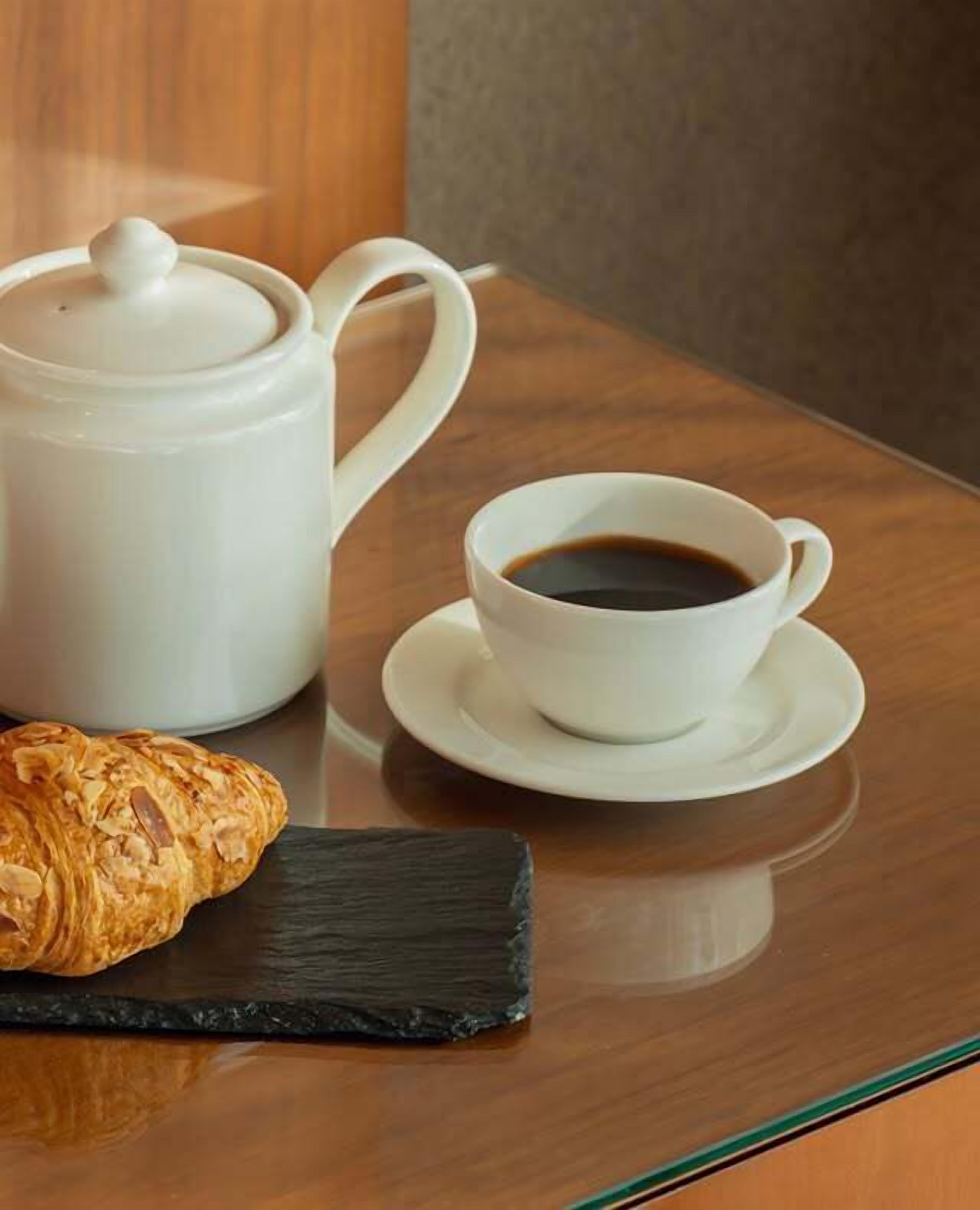 Una bandeja con un croissant, una taza de café y una tetera sobre una mesa de madera.
