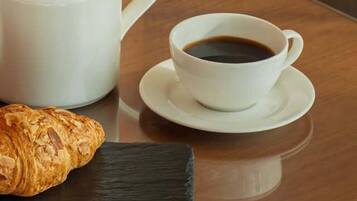 Una bandeja con un croissant, una taza de café y una tetera sobre una mesa de madera.