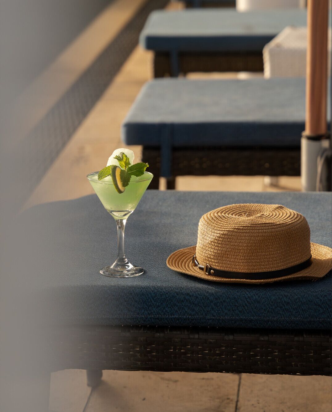 A cocktail in a martini glass with mint leaves on a blue lounge chair.