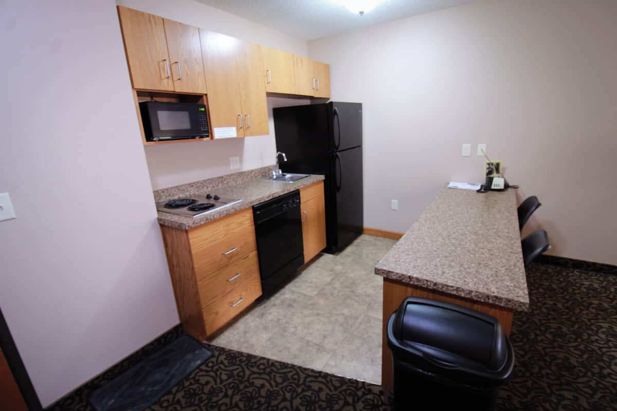 A compact kitchen with wooden cabinets, a black refrigerator, a microwave, and a dishwasher.