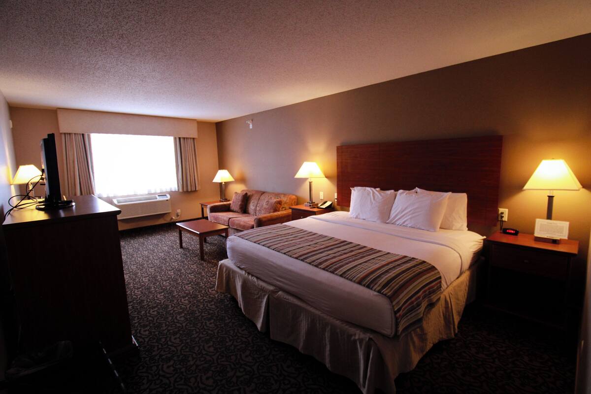 A hotel room with a large bed, a desk, a chair, and two lamps.