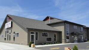A hotel with a modern design, featuring a prominent 'Hotel' sign and a 'Guest Services' sign. It has a sloped roof and a mix of siding and stone accents. - Canby Inn And Suites (Canby)