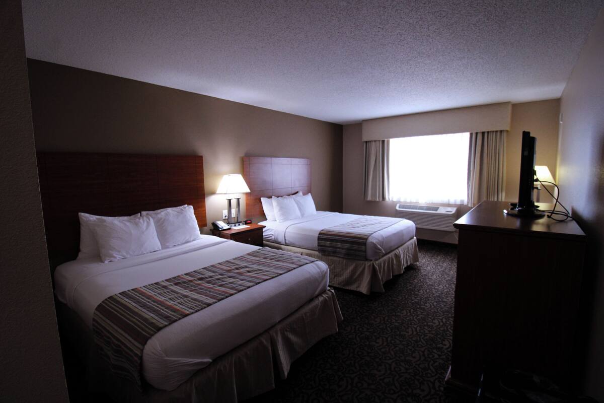 A hotel room with two beds, a desk, a lamp, and a television.