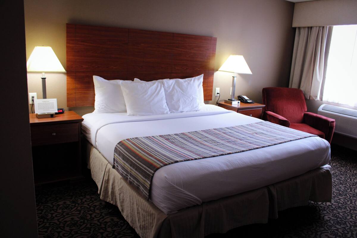 A hotel room with a large bed, two bedside lamps, a red chair, and a window with curtains.