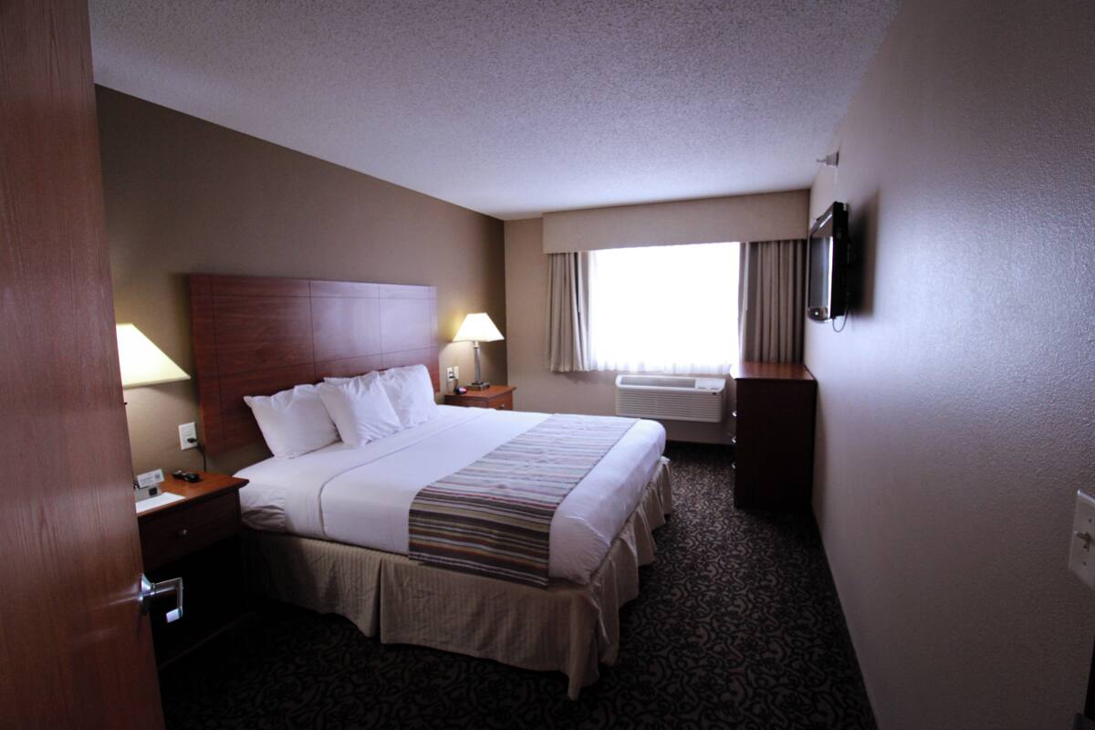 A hotel room with a large bed, two bedside tables, a TV mounted on the wall, and a window with curtains.