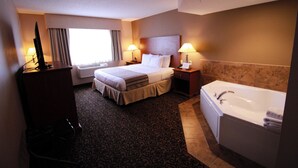 A hotel room with a bed, bedside lamps, a desk with a computer, a large window with curtains, and a bathtub. - Canby Inn And Suites (Canby)