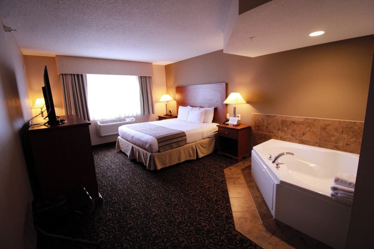 A hotel room with a bed, bedside lamps, a desk with a computer, a large window with curtains, and a bathtub.