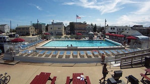 A swimming pool with lounge chairs and umbrellas, surrounded by buildings. - Sea Spray Motel (Beach Haven)