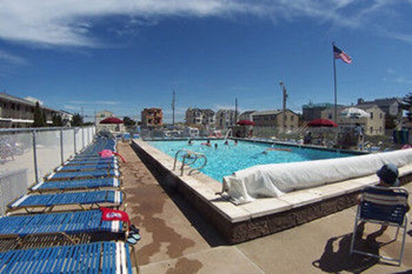 A swimming pool with lounge chairs and a covered area, surrounded by buildings and a flag. - Sea Spray Motel (Beach Haven)