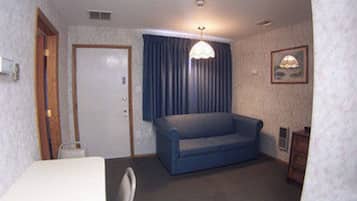 A hotel room with a bed, a blue sofa, a desk, a chair, a lamp, a picture on the wall, and a door.