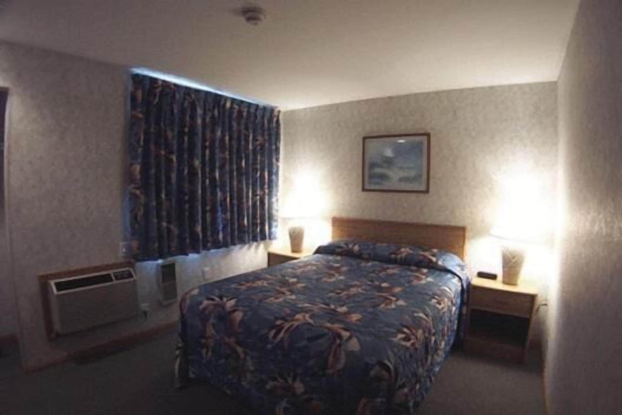 A hotel room with a bed, a nightstand, a lamp, a window with curtains, and a picture on the wall.