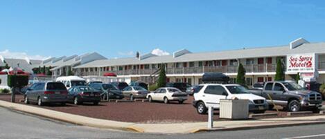 Un motel avec une rangée de chambres, un parking et une enseigne indiquant « Sea Spray Motel ».