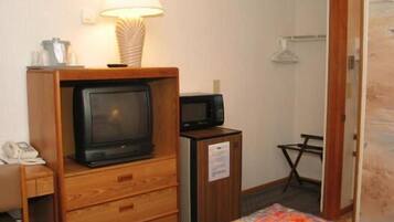 Una habitación de hotel pequeña con un aparador de madera, televisión, microondas, cama con colcha estampada y una lámpara.
