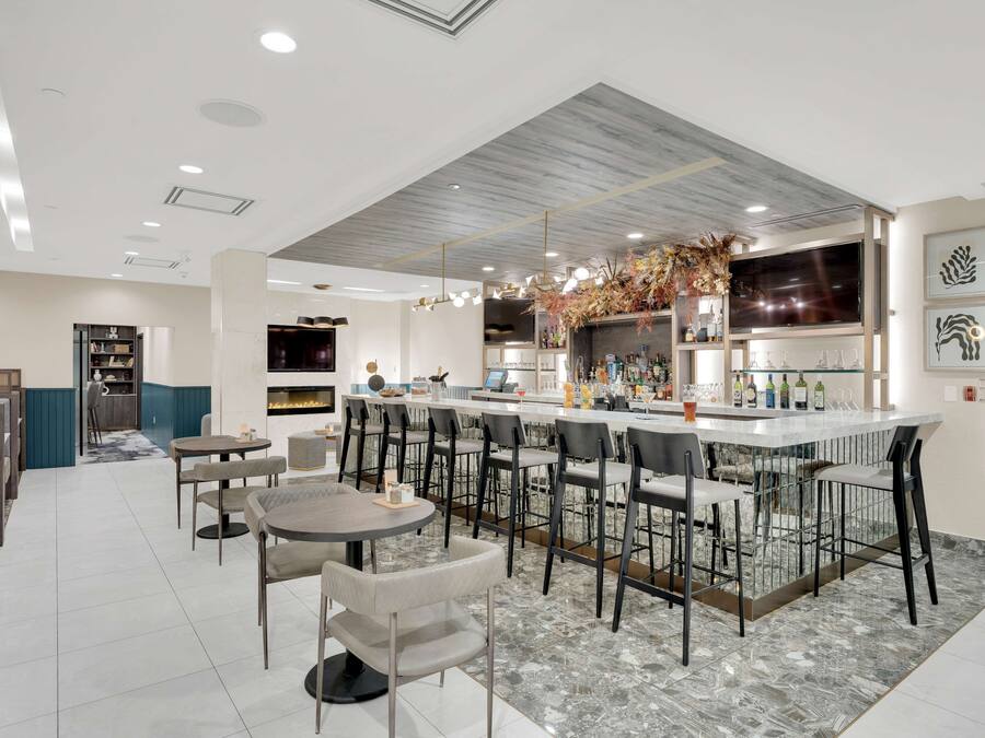 A modern bar area with a marble countertop, bar stools, and a television screen.