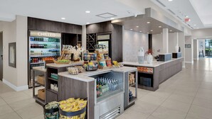 A modern hotel lobby with a chilled beverage fridge, a frozen section, and a variety of snacks and beverages on display.
