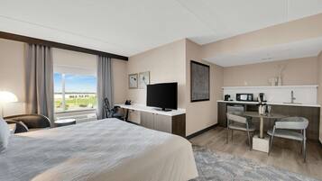 Ett hotellrum med en stor säng, ett skrivbord med en tv, ett litet kök och utsikt över omgivningarna.