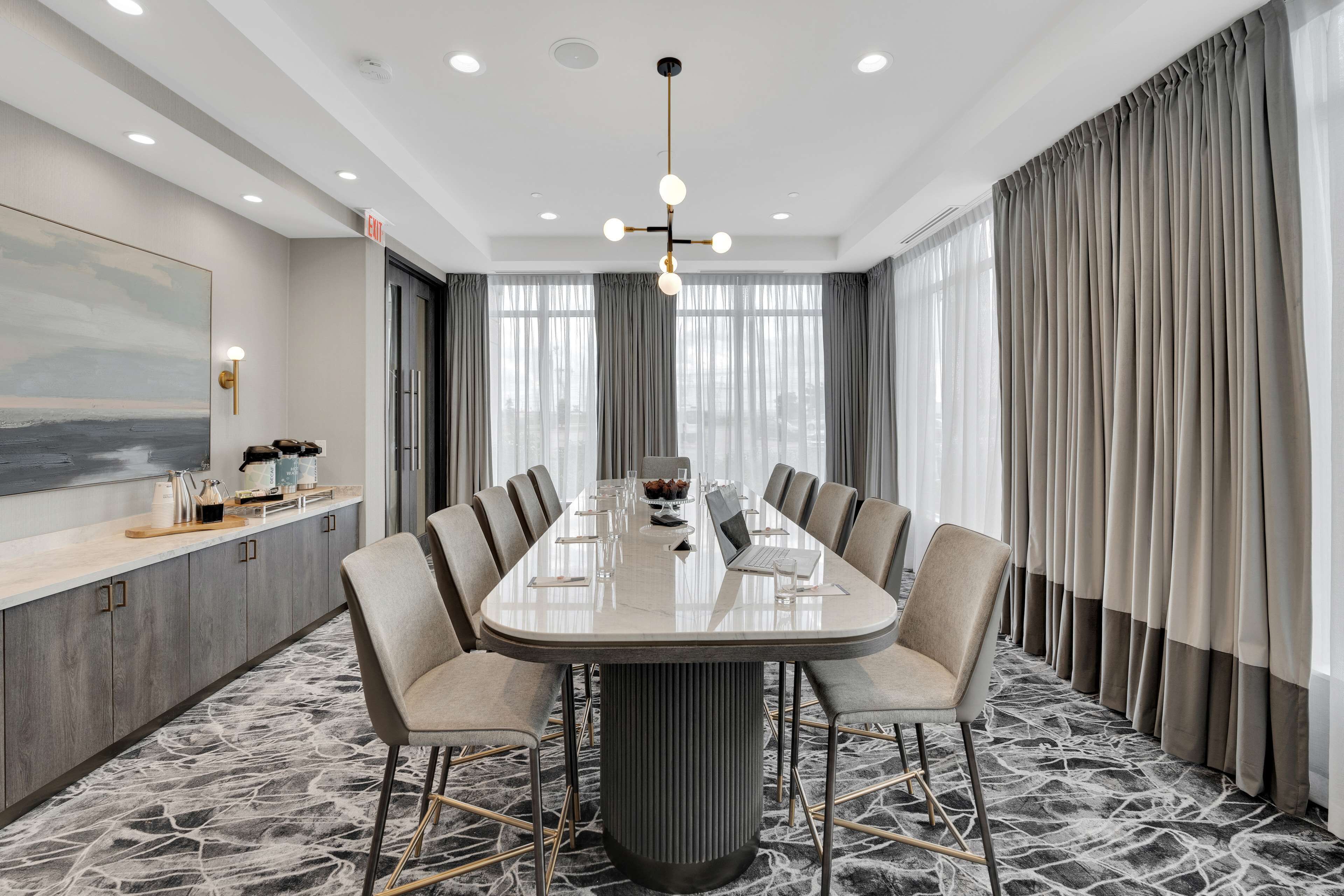 A conference room with a large oval table, grey curtains, and a modern chandelier.