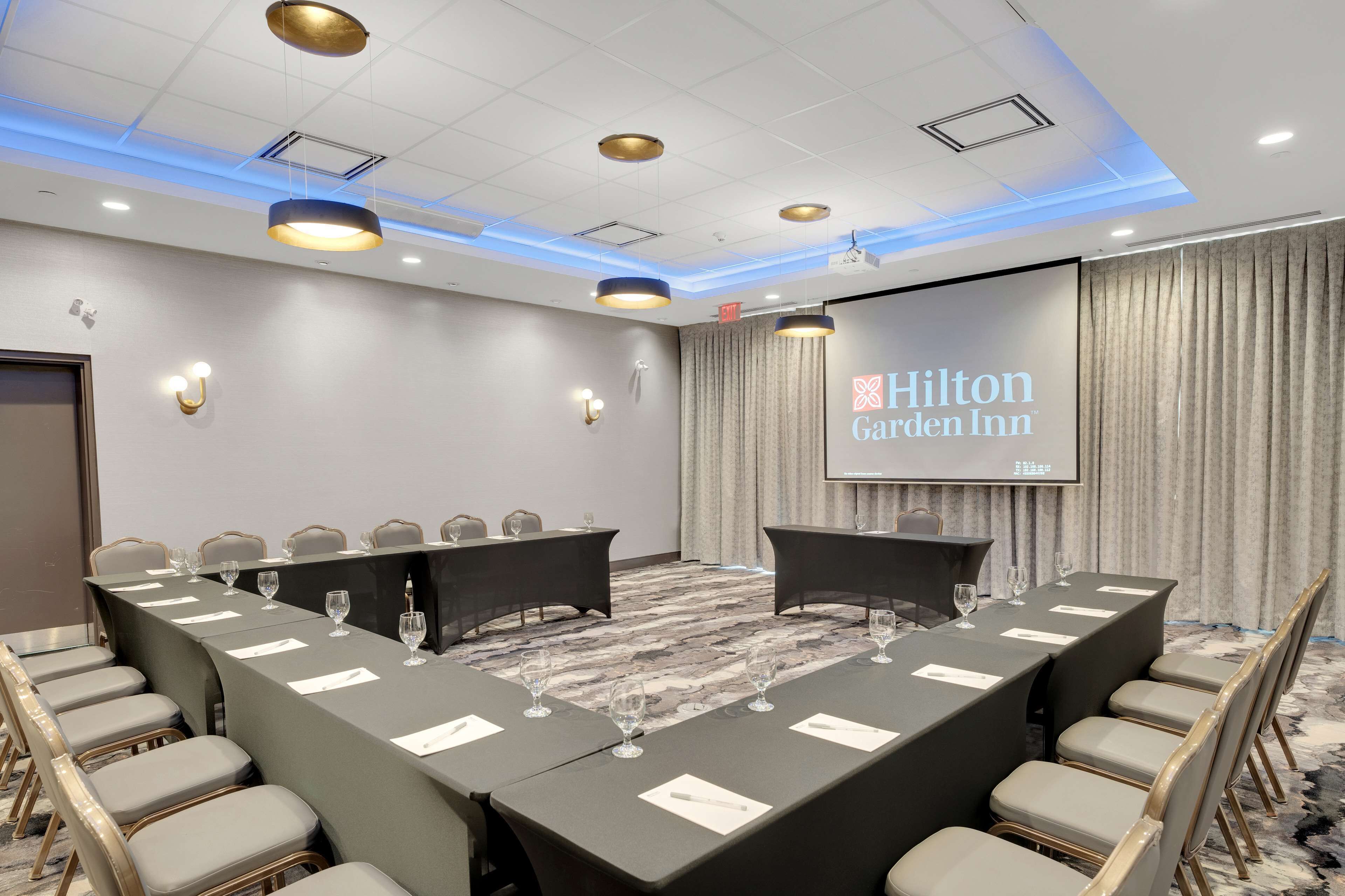Kokoushuone, jossa on pitkä pöytä, tuoleja ja näyttö, jossa näkyy teksti ”Hilton Garden Inn”.