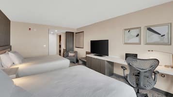Quarto de hotel com duas camas, uma escrivaninha, uma cadeira, televisão e quadros na parede.
