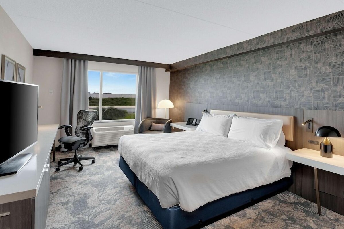 A hotel room with a bed, desk, chair, TV, and a view of the outdoors.