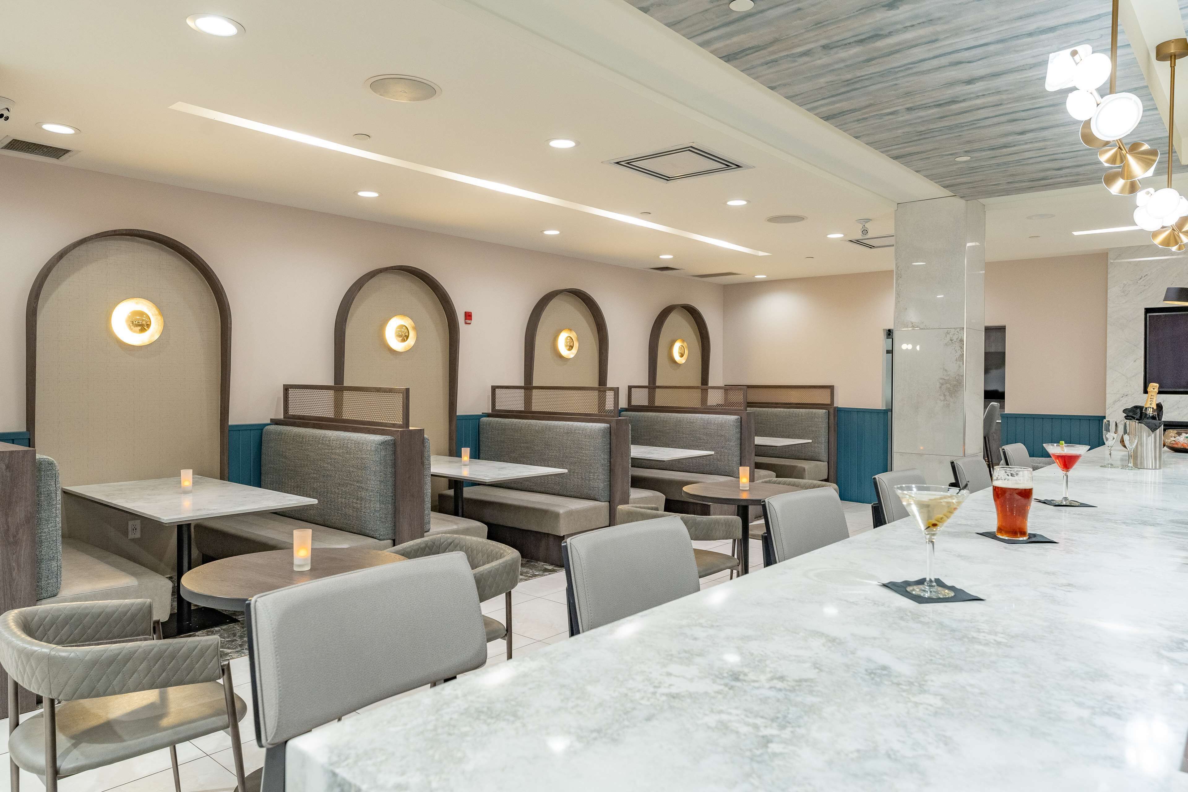 A restaurant with booths and tables, a marble bar area, and recessed lighting.