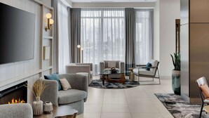 A modern living room with a flat-screen TV, comfortable seating, a fireplace, and large windows with curtains.
