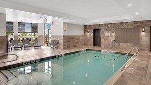An indoor swimming pool with clear lane markings, a shallow area sign, and a seating area with chairs and a table.