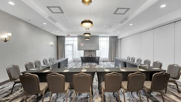 A conference room with a long table, multiple chairs, and a large screen displaying the Hilton Garden Inn logo.